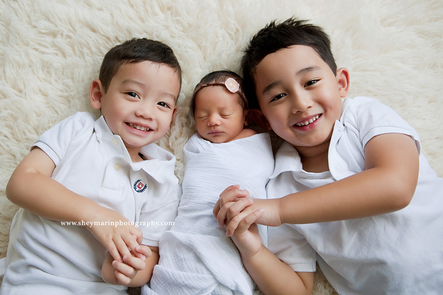Three siblings smiling with newborn