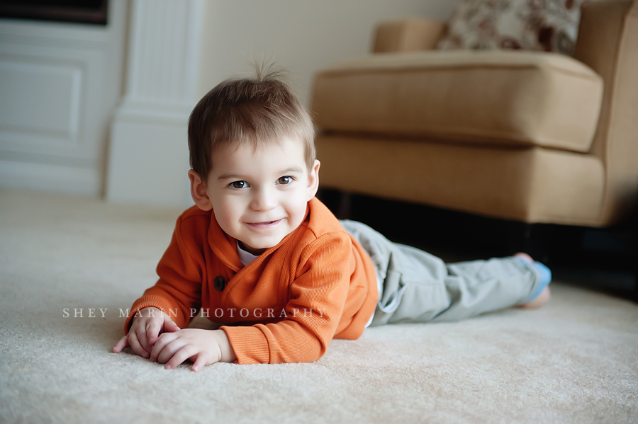 Toddler boy in orange smiling on floor