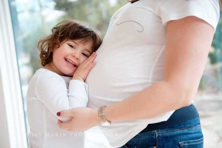 toddler girl hugging mom's pregnant belly in Frederick, MD