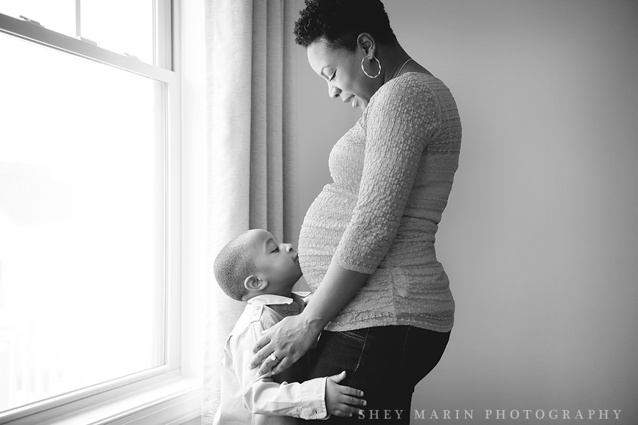 black and white maternity photo with brother kissing belly