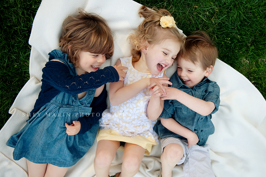 three toddlers laughing on a blanket in the grass