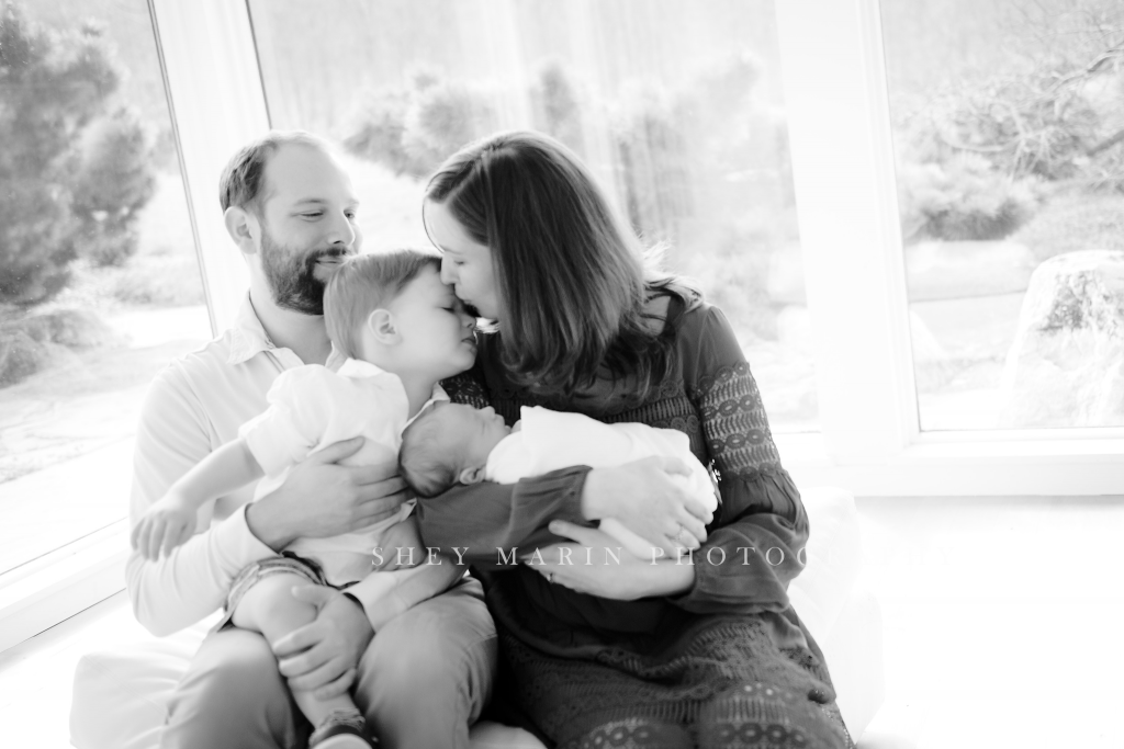 black and white photo of family kissing newborn