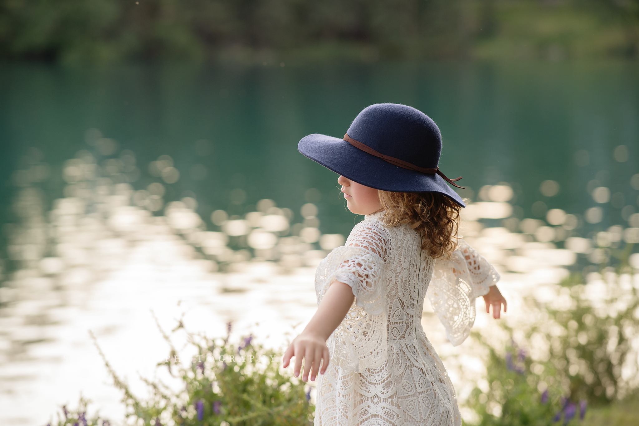 travel family photo session girl in lace dress by lake spinning with hat