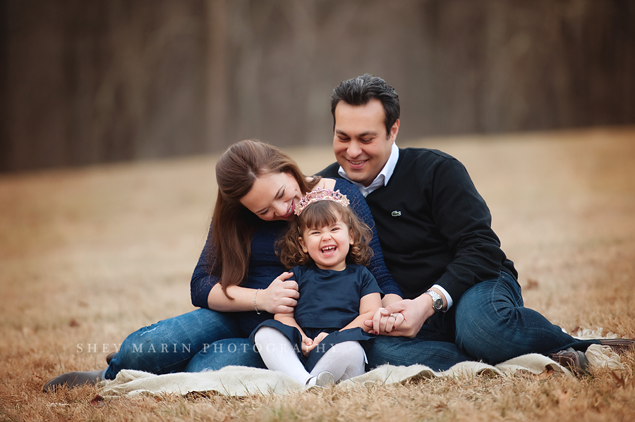 winter maternity photo session with family on blanket smiling and laughing