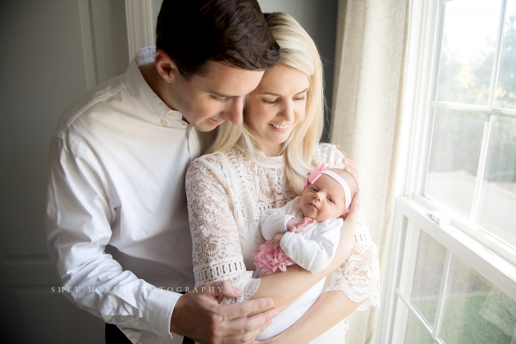 new baby girl with mom and dad in window light in Maryland