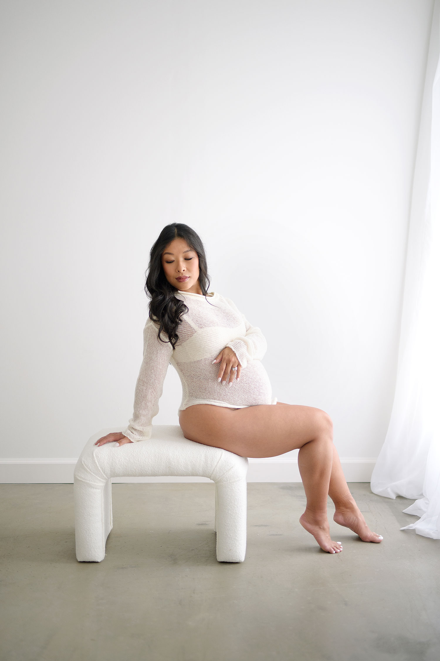 beautiful pregnant photo of woman sitting on a bench in a photography studio for her maternity session.